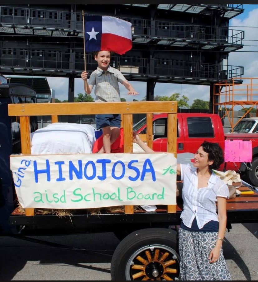 Gina and her son waving a Texas flag and standing with a sign that says "Gina Hinojosa for AISD school board"